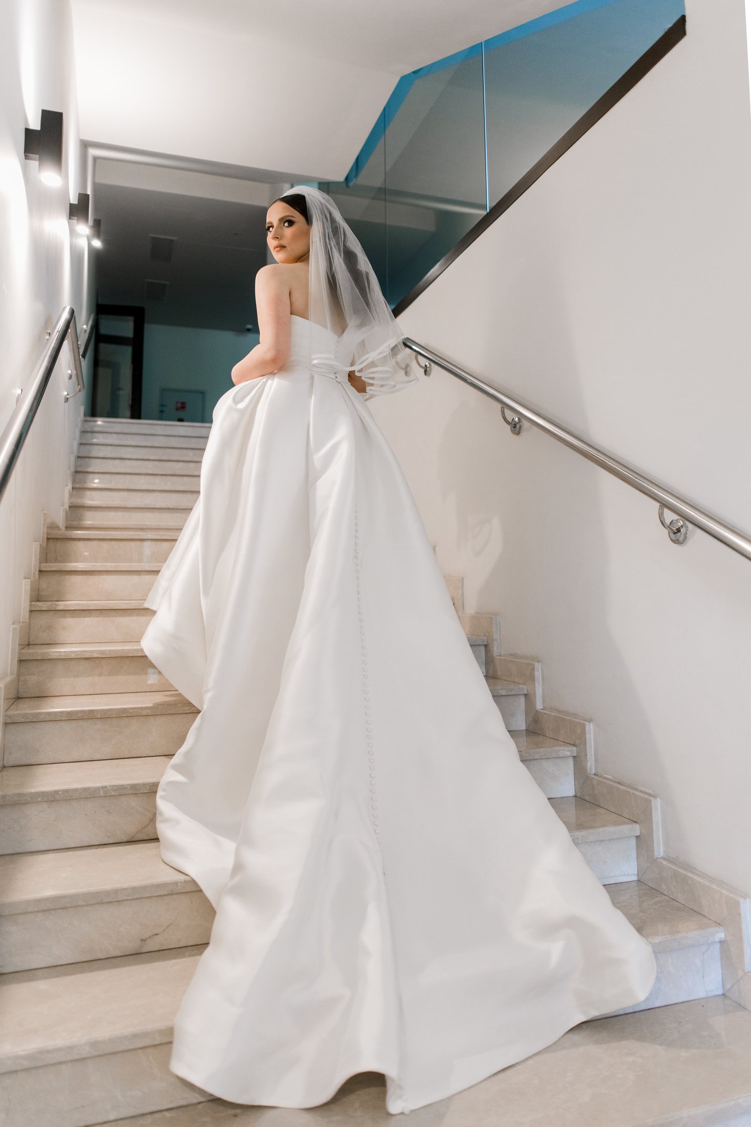 Bride in a white wedding gown ascending a modern staircase